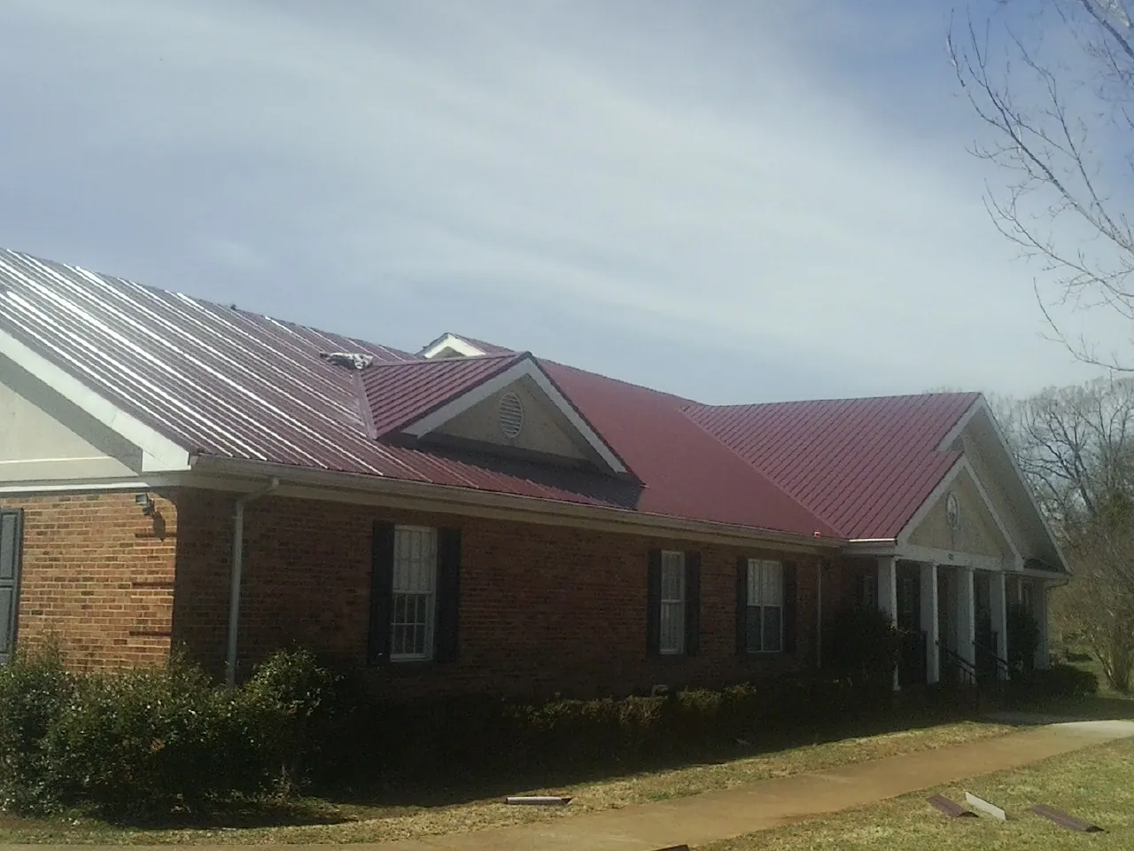 Red metal roof with gabled entries on a long brick building, from a Hail Damage Roof Repair job in Port Hadlock