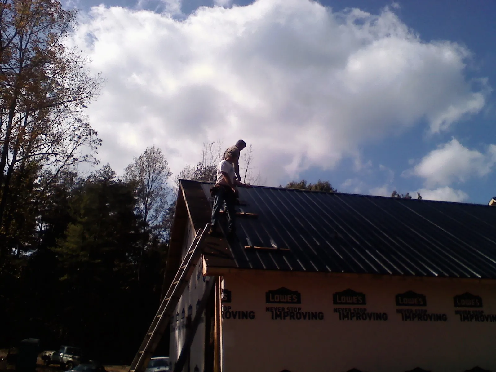 Roofer fastening dark metal panels high against a cloudy sky, from a Roof Inspection job in Port Hadlock