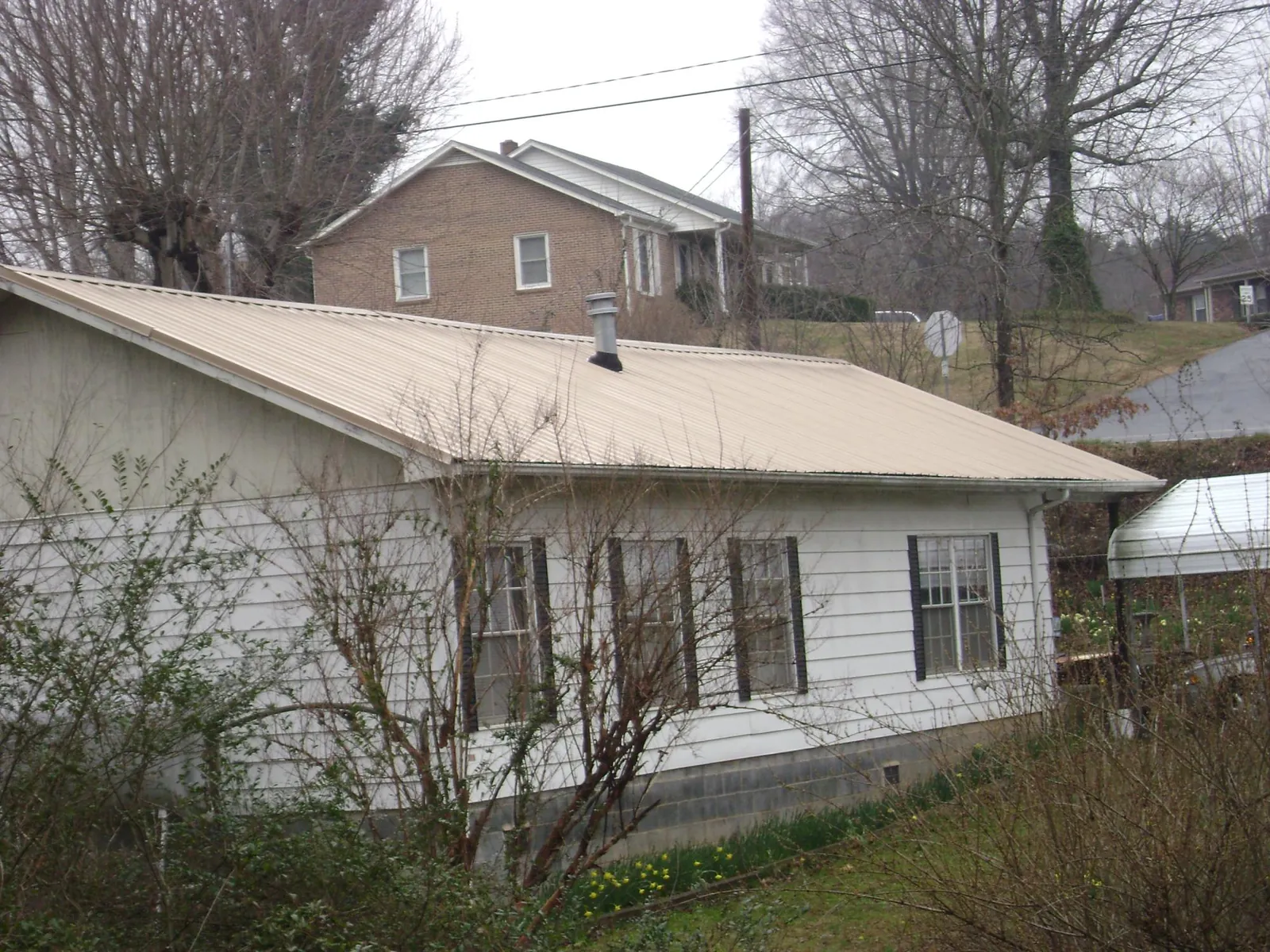 Tan metal roof on a white sided house set into a hillside — Commercial Roofing by Roofing Brothers in Port Hadlock